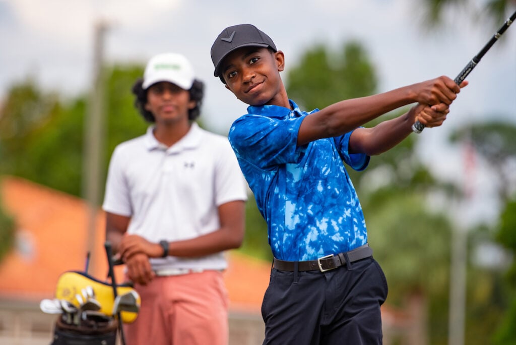 Smiling First Tee junior golfer in a blue polo finishing his swing.
