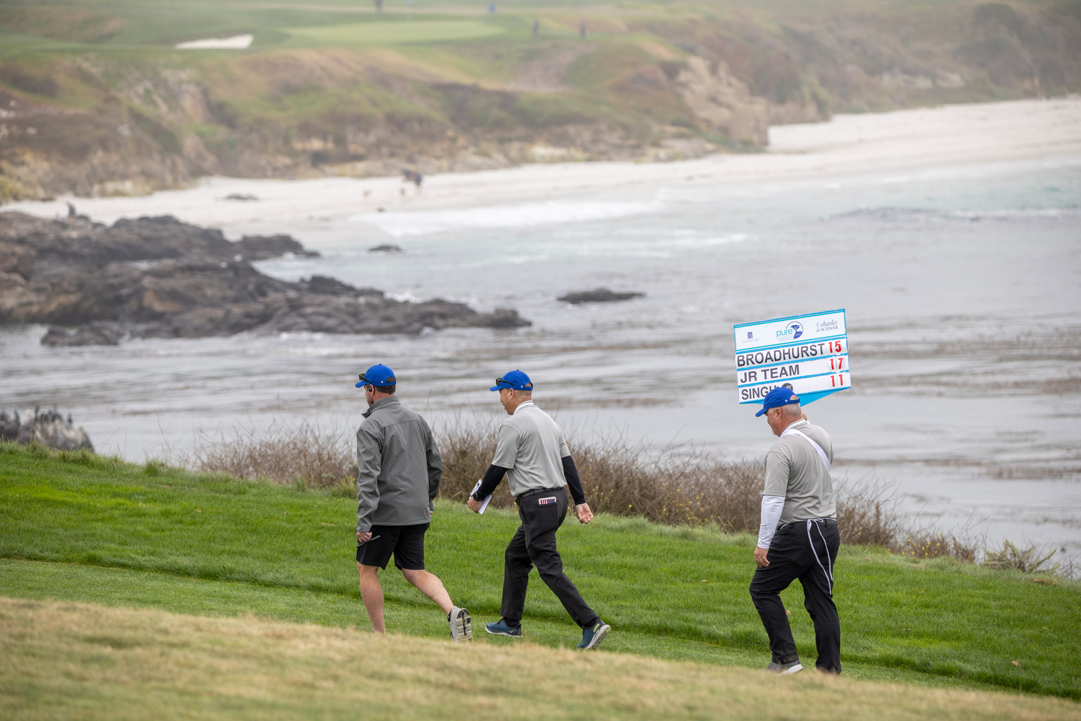 Two female tournament volunteers in grey jackets and caps smiling together on a lush green course