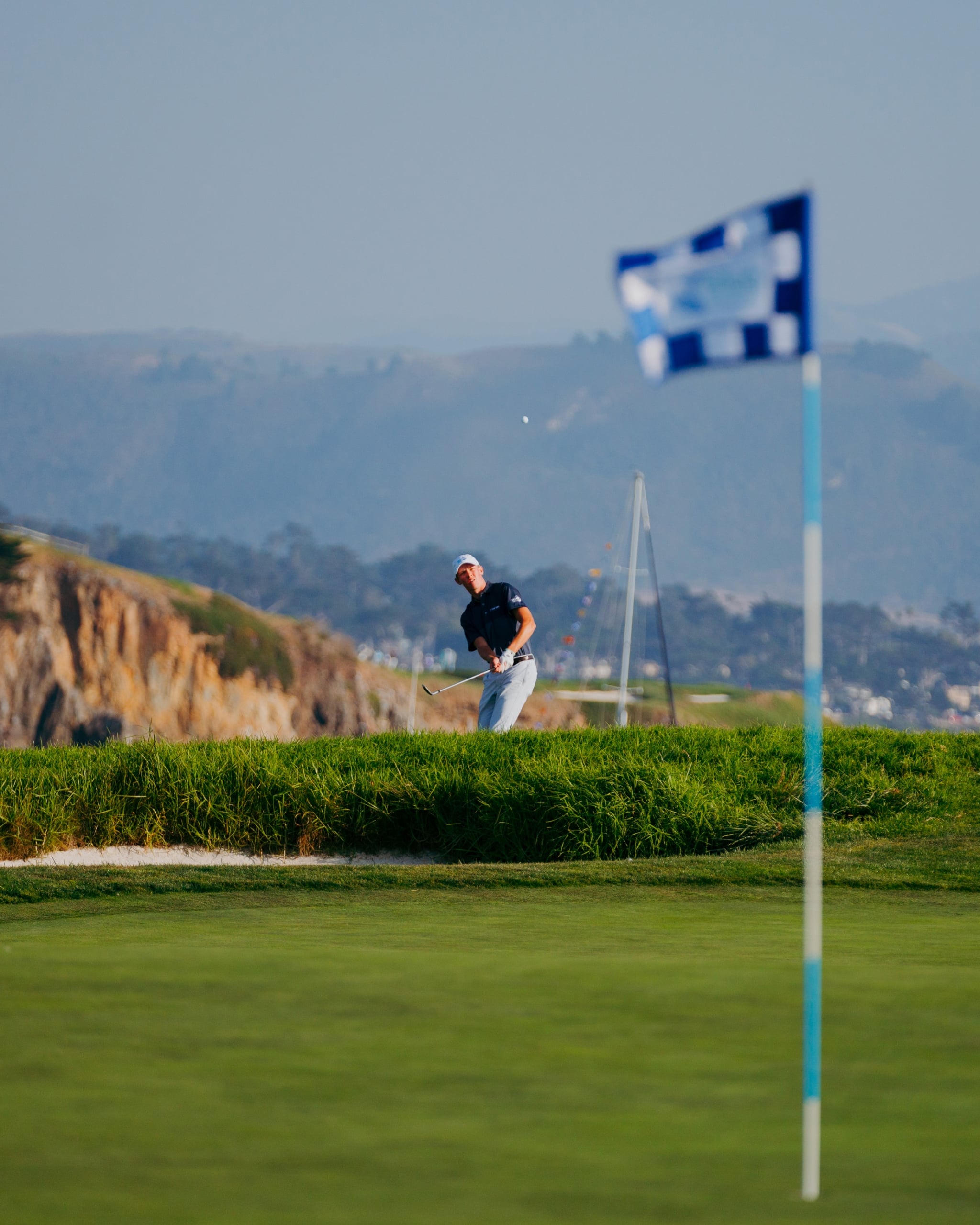 A young golfer watches his ball fly after a shot from the rough overlooking the coastline