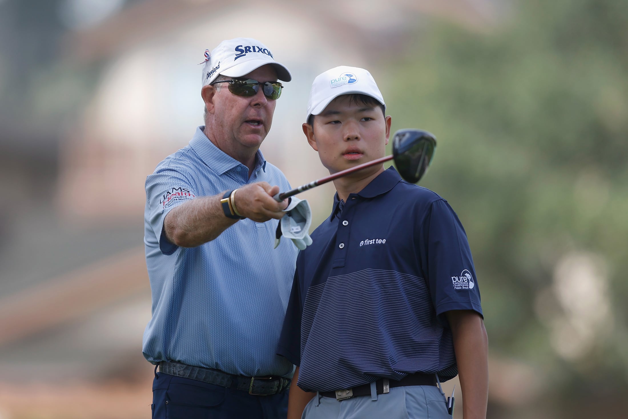 A professional golfer points toward the fairway while mentoring a young First Tee participant on the tee box