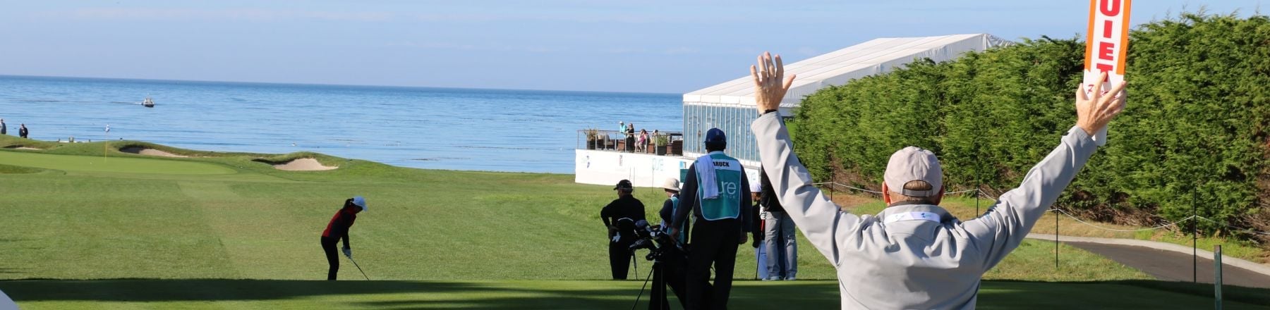 Volunteer holding orange signal paddles as a golfer tees off toward the ocean at Pebble Beach