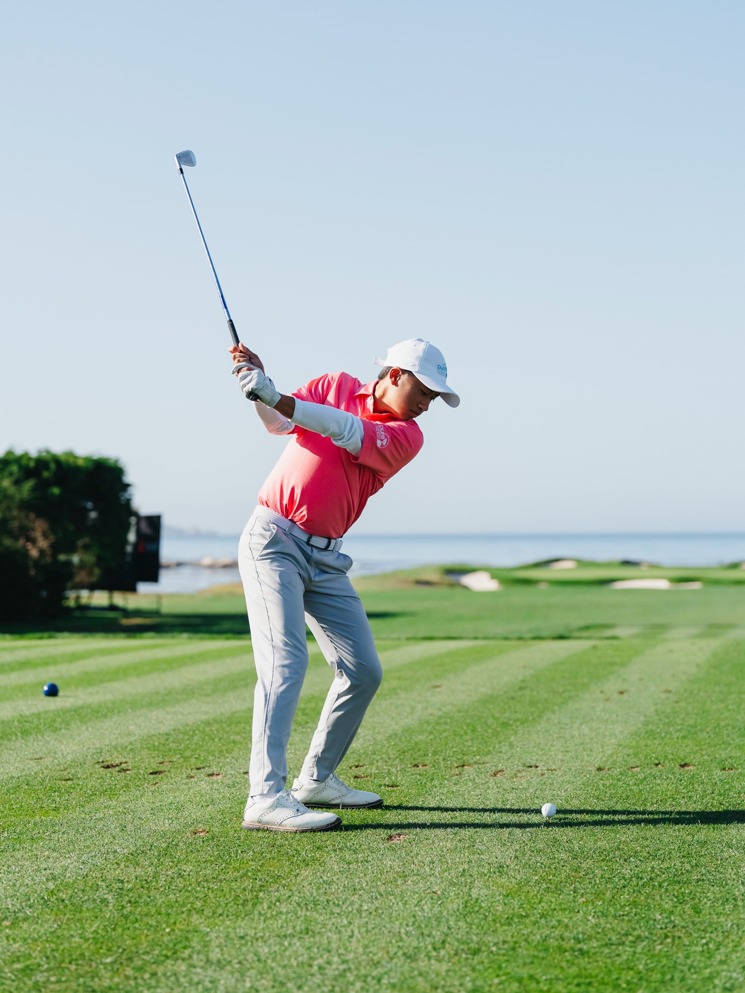 A junior golfer in a bright pink polo mid-swing on a perfectly manicured green fairway