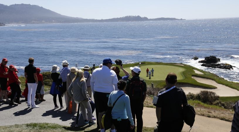 Spectators gathered on a hill overlooking a green situated on a rocky point at Pebble Beach