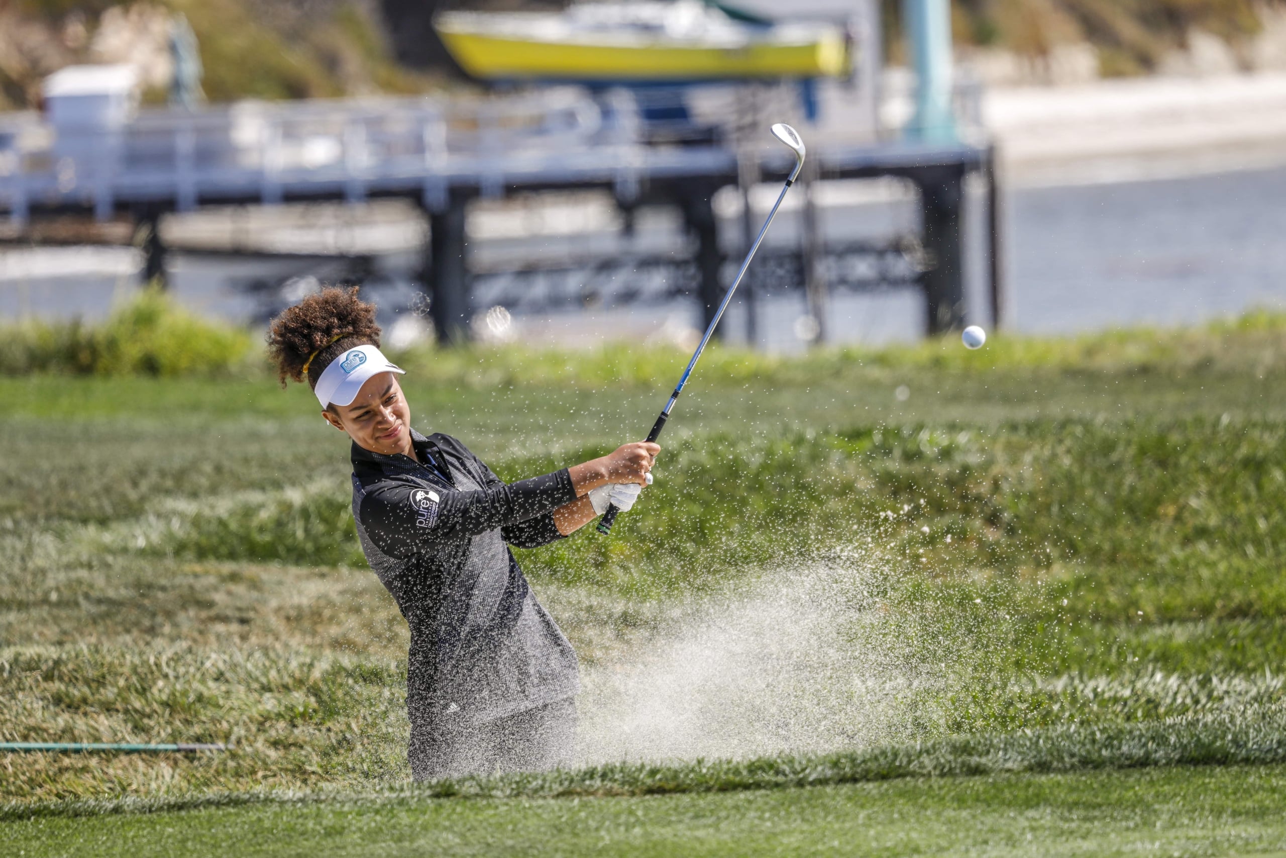 Action shot of a young female golfer blasting her ball out of a sand bunker near the water