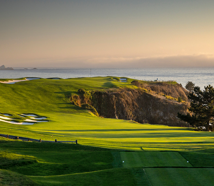 Golden hour sunlight illuminates a cliffside green and rolling fairways along the Pebble Beach coast