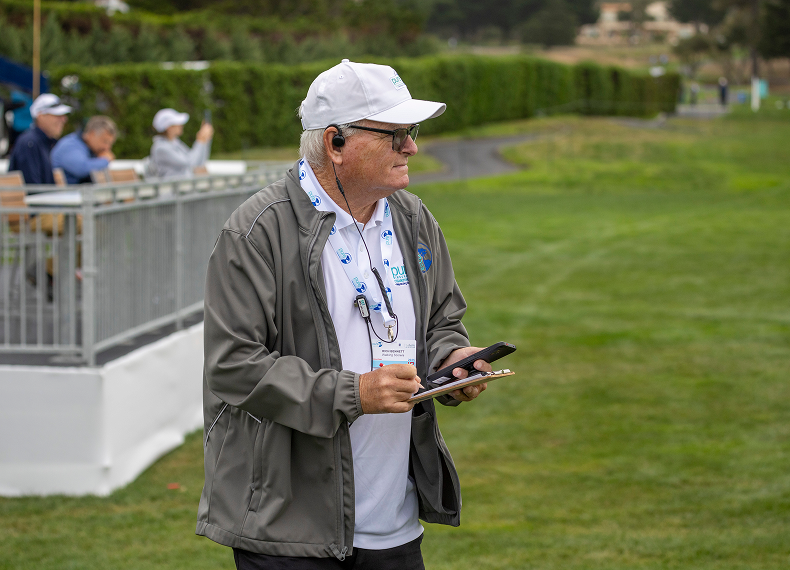 Walking scorer Rich Bennett recording tournament data on a clipboard and mobile device during play