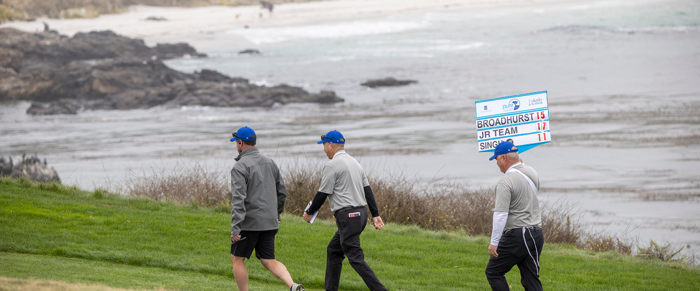 Tournament officials walk along a grassy ridge overlooking a rocky, wave-swept beach