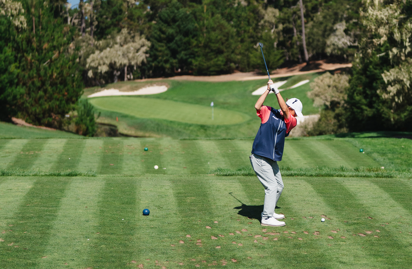 Junior golfer in a First Tee vest mid-backswing at Pebble Beach.
