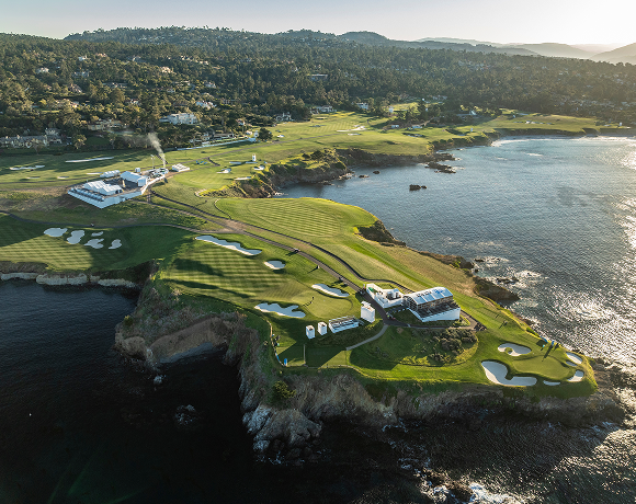 High aerial view of a coastal golf course with fairways, greens, and white tents along the cliffs