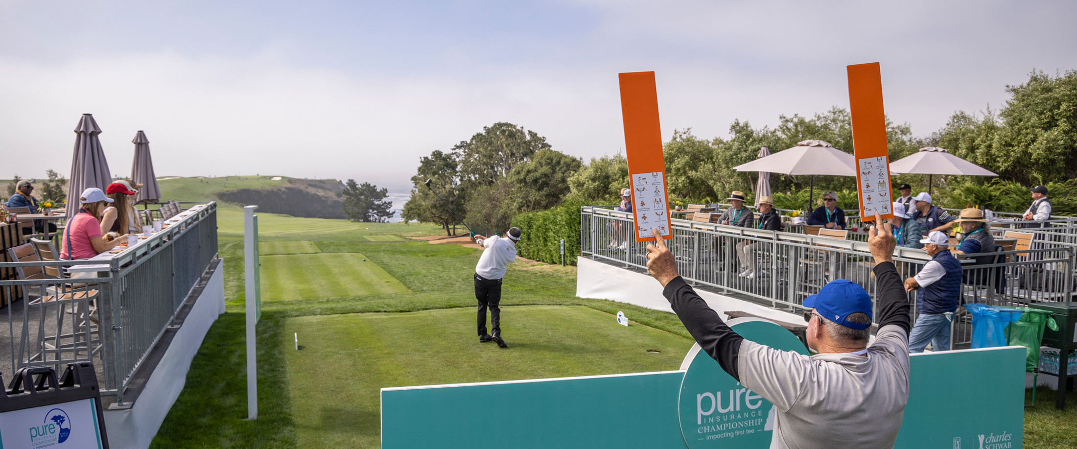 Volunteer raising orange paddles to signal ball flight as a golfer tees off for spectators at Pebble Beach