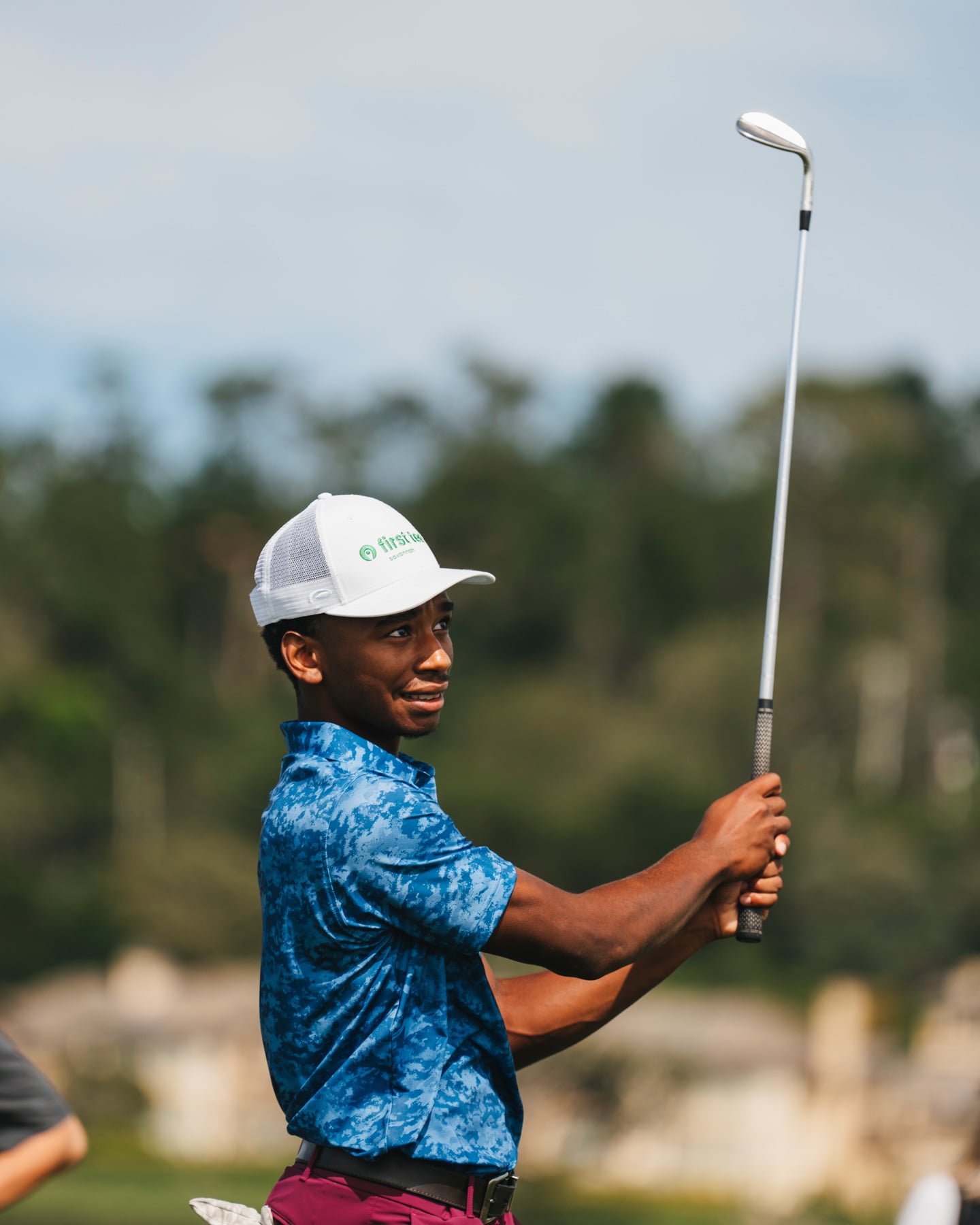 Close-up of a young First Tee golfer in a blue patterned polo holding a golf club and looking off-camera