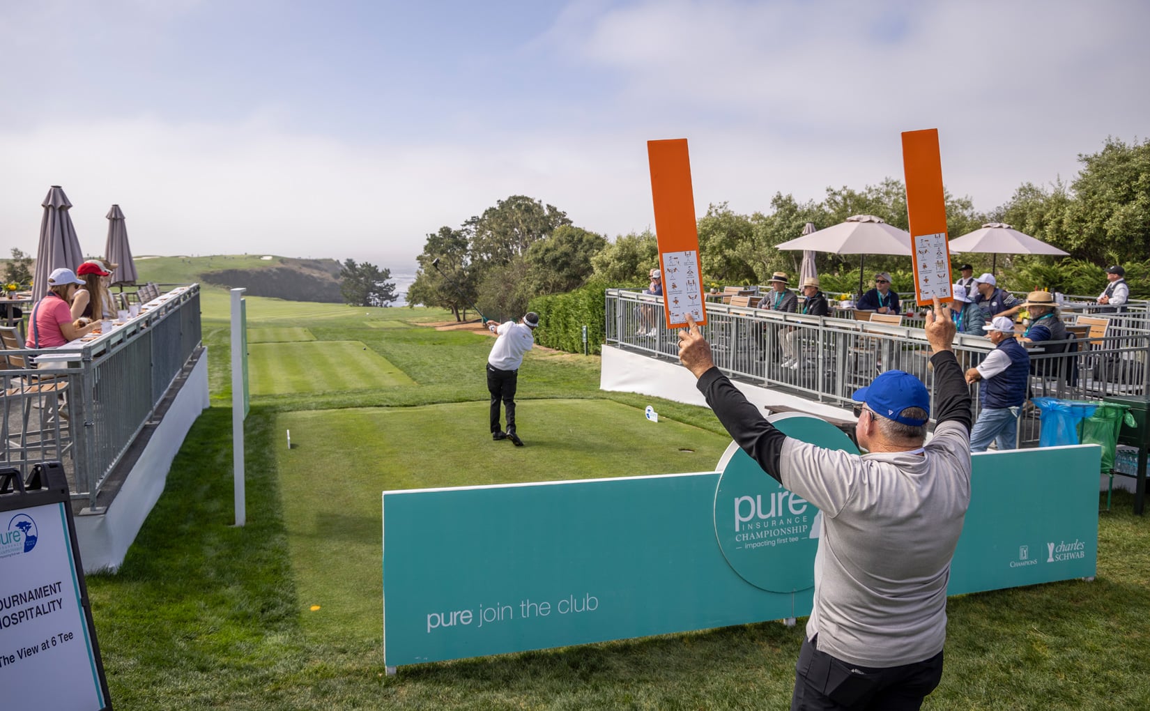 Volunteer using orange paddles to track a tee shot toward the ocean at Pebble Beach